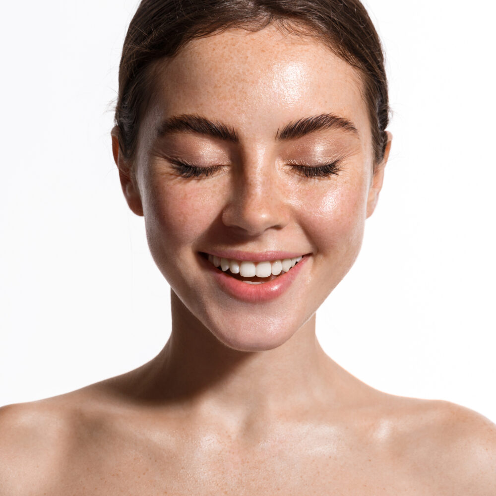 A white woman with short red-brown hair smiles while closing her eyes.