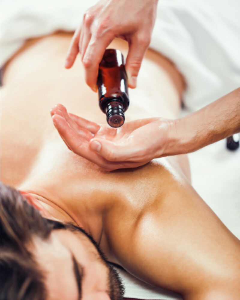 A masseuse dropping oil into their hands over a white man's back during a massage.