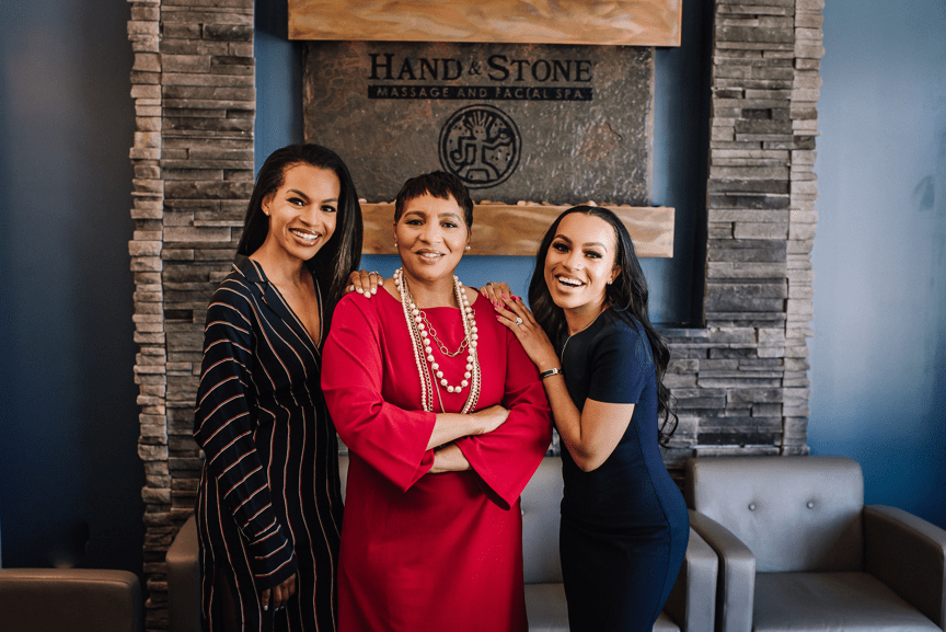 Franchisee and two daughters standing in front of hand & stone sign